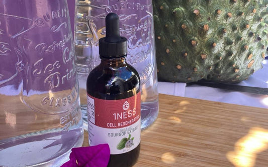 A 1NESS soursop extract bottle in front of glass water bottles and a whole soursop fruit on a wooden table